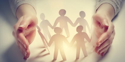 Paper people surrounded by hands in gesture of protection. Concept of insurance